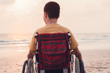 The back of a handicapped child in a wheelchair on the beach at sunset, Diverse People concept ,...
