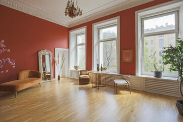 antique vintage interior in 19th century style living room with bright red walls, wood floor and direct sunlight inside the room.