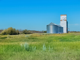 Abandoned grain elevator and grain storage bins near a field of wheat on the Canadian prairies near...