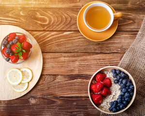 strawberries, blueberries and oatmeal in the bowl, cup of tea and lemon  on wooden background