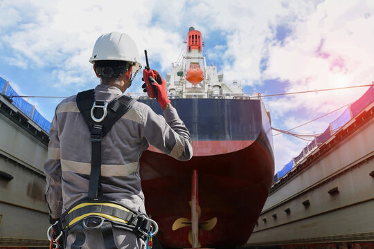 foreman, supervisor, port controller, wearing equipment safety harness loading master in charge of working in the dry dock, control and communication to the teamwork by walkie talkie radio in shipyard
