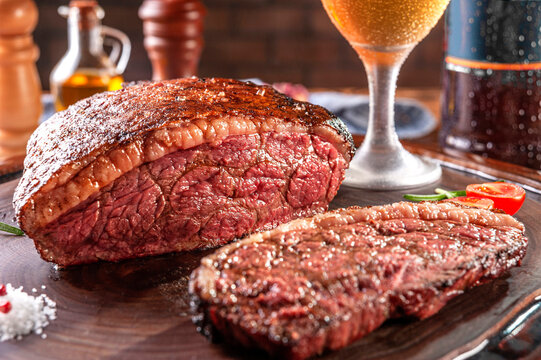 Grilled sliced cap rump steak with two glasses of beer on wooden cutting board. Marble meat beef (Brazilian picanha).