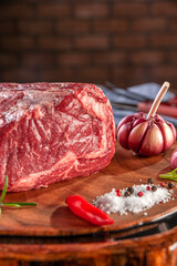 Raw entrecote beef on a wood cutting board with spices on bricks wall background - Closeup.