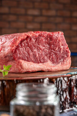 Raw strip loin beef (argentine chorizo) on a wood resined cutting board. Wooden table with bricks wall background - Closeup.
