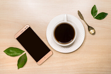 Fototapeta na wymiar A smartphone, a mug of coffee and a spoon lie on the table obliquely.