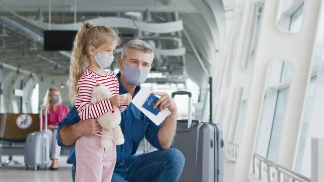 Senior father and his lovely daughter wearing protective masks looking at airplanes through the glass window and chatting with pleasure emotions. Travel during the pandemic with baby concept