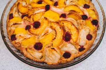 Delicious, fresh, baked pie made of apples, piers, raspberries close-up in a round glass form stands on a white table. Photography, concept.