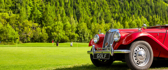 Golfers on the green, the forest in the background, a red vintage car in the foreground