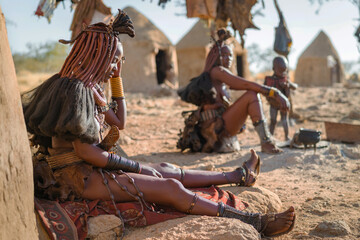 Himba women sitting outside their huts in a traditional Himba village near Kamanjab in northern Namibia, Africa. - obrazy, fototapety, plakaty