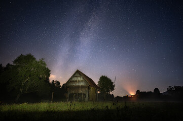 Fototapeta na wymiar Milky way over a traditional Slovenian barn house (hayloft) in the night sky
