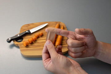 Close-up of a wound patch on a finger. cut into the finger while cooking. Care bloody wound at home. in the background is a cutting board, a knife and carrots. 