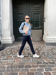 Obraz premium Woman wearing sunglasses going to work holding magazine against the green wall and the city