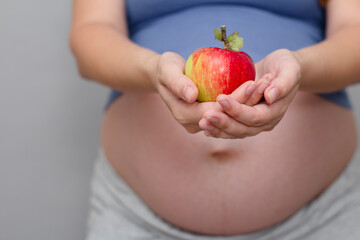 Pregnant woman holding apple on gray studio background , healthy pregnancy concept