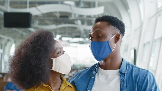 Portrait shot of the young multiracial happy couple wearing protective masks standing in the airport hall and smiling joyfully to the camera