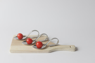 Red sweet candy tomato in metallic snack spoon on wooden plate.