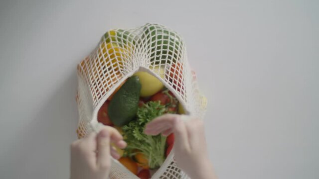 healthy eating, organic fresh fruits and vegetables in reusavle bag. female hand with eco bag on white background. zero waste concept. eco bag made from natural cotton fabric