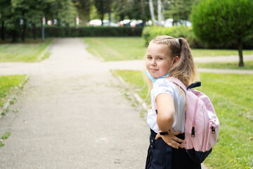 blonde curly schoolgirl puts of protective mask in school uniform with pink backpack back to school