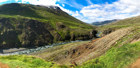 Summer Iceland panorama on winding river among fields and hills of green grass.
