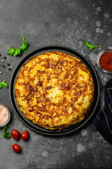 Spanish tortilla with ham and olives in cast iron skillet, dark background. Space for text, top view.