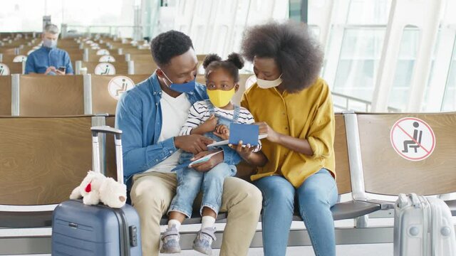 Cute multiracial little girl sitting in the airport with her parents and they looking at their passports, while waiting at their departure