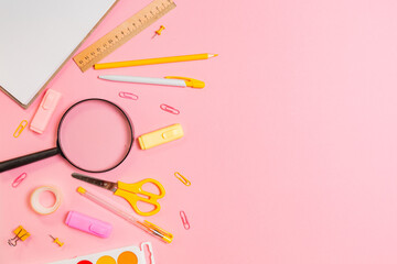 Composition with magnifier, copybook and yellow office supplies on pink background. Flat lay. Copy space. Concept of education and back to school