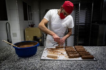 White male pastry chef with cake design haute cuisine cap, hand dipping chocolate cakes. Front view