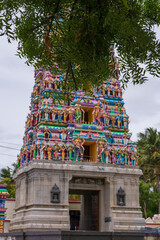 Temple tower in close up with full architecture details. Multi colour temple tower in south India surrounded by the trees...