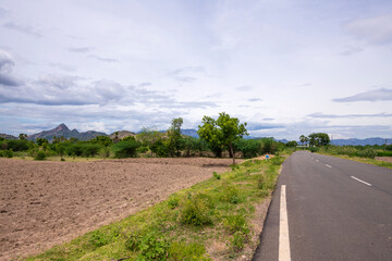 Empty agriculture land , Plowed field, fertile, black - brown soil ready for sowing. Field ready for seeding and planting. Plowed field surrounded by the mountain and palmyra palm - trees...