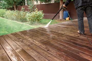 Man cleaning walls and floor with high pressure power washer. Washing terrace wood planks and...