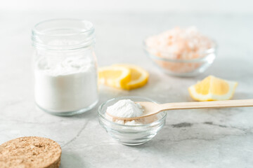 Eco friendly natural cleaners, jar with baking soda, lemon, pink salt and wooden spoon on marble table background. Organic ingredients for homemade cleaning. Zero waste concept.