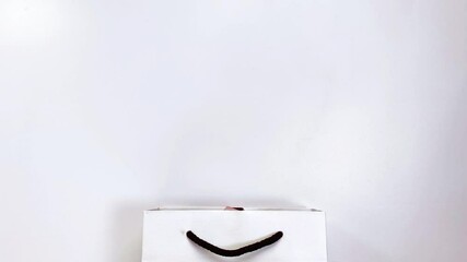 Beauty concept. Stop motion video where makeup products shadows, highlighter, blush, brushes, powder, glitter, mascara, gloss, lipstick, pencil fly into a white gift bag.