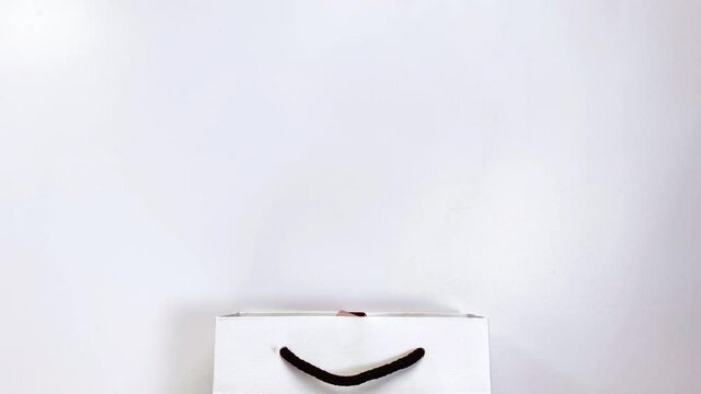 Beauty concept. Stop motion video where makeup products shadows, highlighter, blush, brushes, powder, glitter, mascara, gloss, lipstick, pencil fly into a white gift bag.