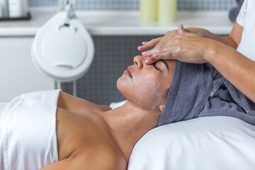 Side view of a beautician applying cream on face of woman in the skin care treatment in spa salon