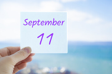 11th September. Hand holding sticker with text September 11 on the blurred background of the sea and sky. Copy space for text. Month in calendar concept