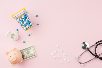 Pills with stethoscope and piggy bank on pink desk