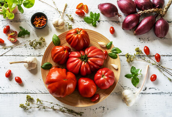 tomatoes on the plate and white wooden background with oregano, basil leaves, garlic and onion