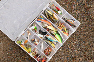 A fishing tackle box filled with lures, wobblers and fishing equipment lying on the sand