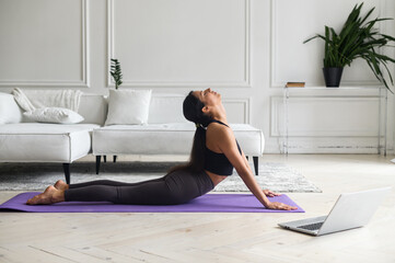 Concentrated young mindful indian woman in sportswear practicing yoga and watch online tutorial on...