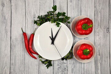 Lunch time. Kitchen clock and red Bulgarian and Chilean peppers on a gray background.