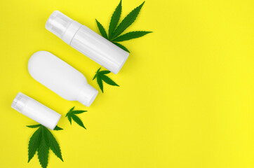 Hemp cosmetics and green hemp leaves on a yellow background. Natural hemp cosmetics. Natural body care