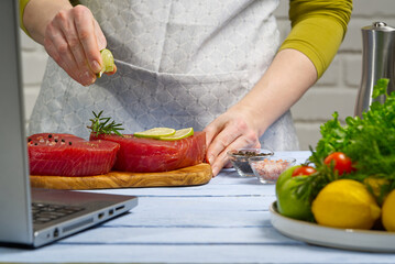 cooking woman in kitchen with pc looking how to cook tuna fish. cooking and computer laptop concept.