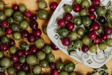 Green and red gooseberries. Gooseberries on a wooden surface and on a white plate. Plate with gooseberries