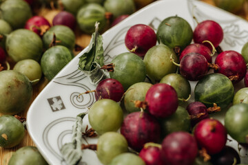 Green and red gooseberries. Gooseberries on a wooden surface and on a white plate. A plate with gooseberries. Dry mint leaf