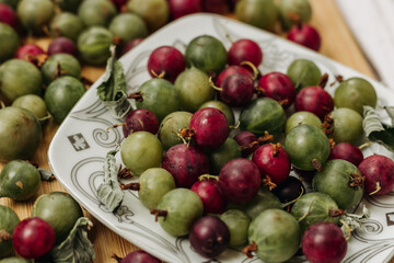Green and red gooseberries. Gooseberries on a wooden surface and on a white plate. A plate with gooseberries. Dry mint leaf