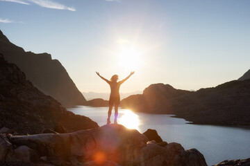 Adventurous Caucasian Adult Woman Hiking on top of a Canadian Rocky Mountain with hands up. Sunny...
