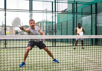Athletic mens plays padel. View through the tennis net