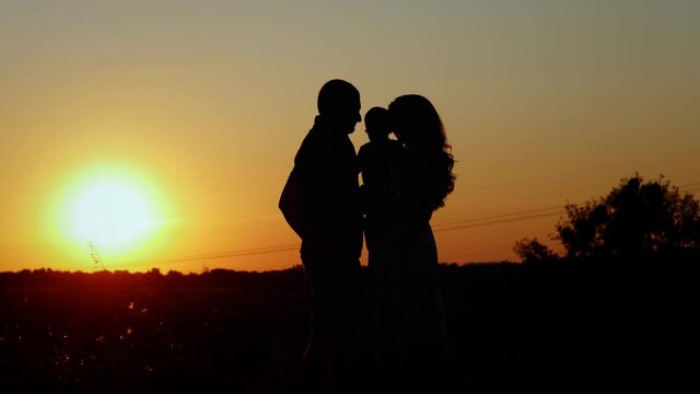 Parents kiss and hug their baby, unrecognizable silhouette of a family at sunset, family values and parental love