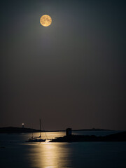 super moon or blood moon shining and reflecting its lights on a docked sailboat at midnight in the...