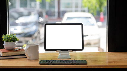 Workspace blank white screen tablet with coffee mug keyboard placed at a wooden table by the mirror at the office. Mock up.