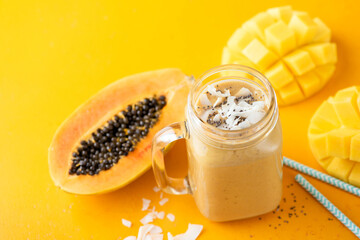 Tropical mango papaya smoothie in glass jar on yellow background. Vegan fruit smoothie